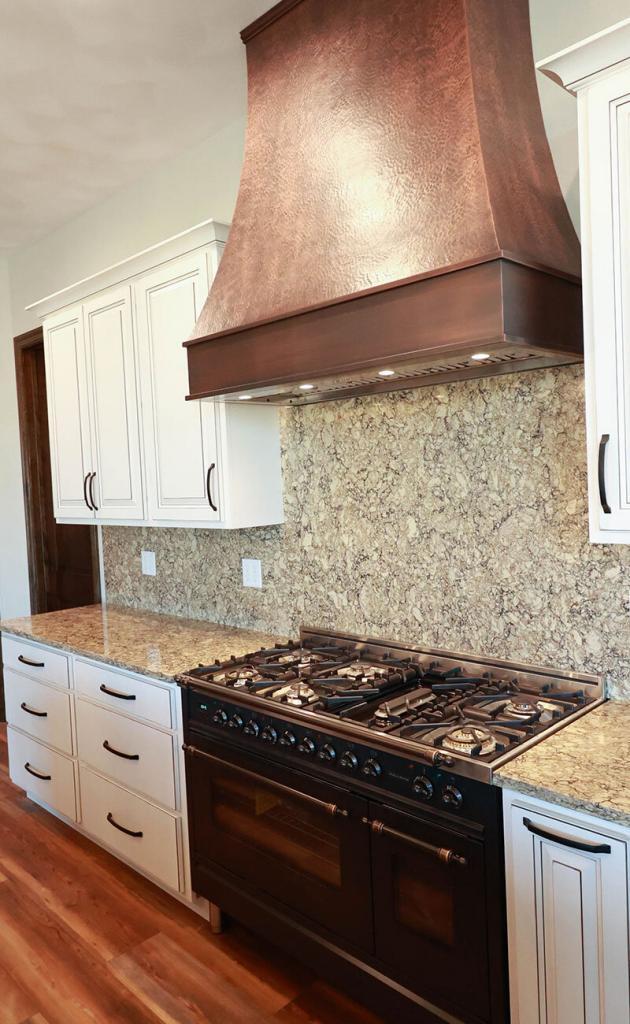 white kitchen cabinets with quartz counters and a copper hood vent